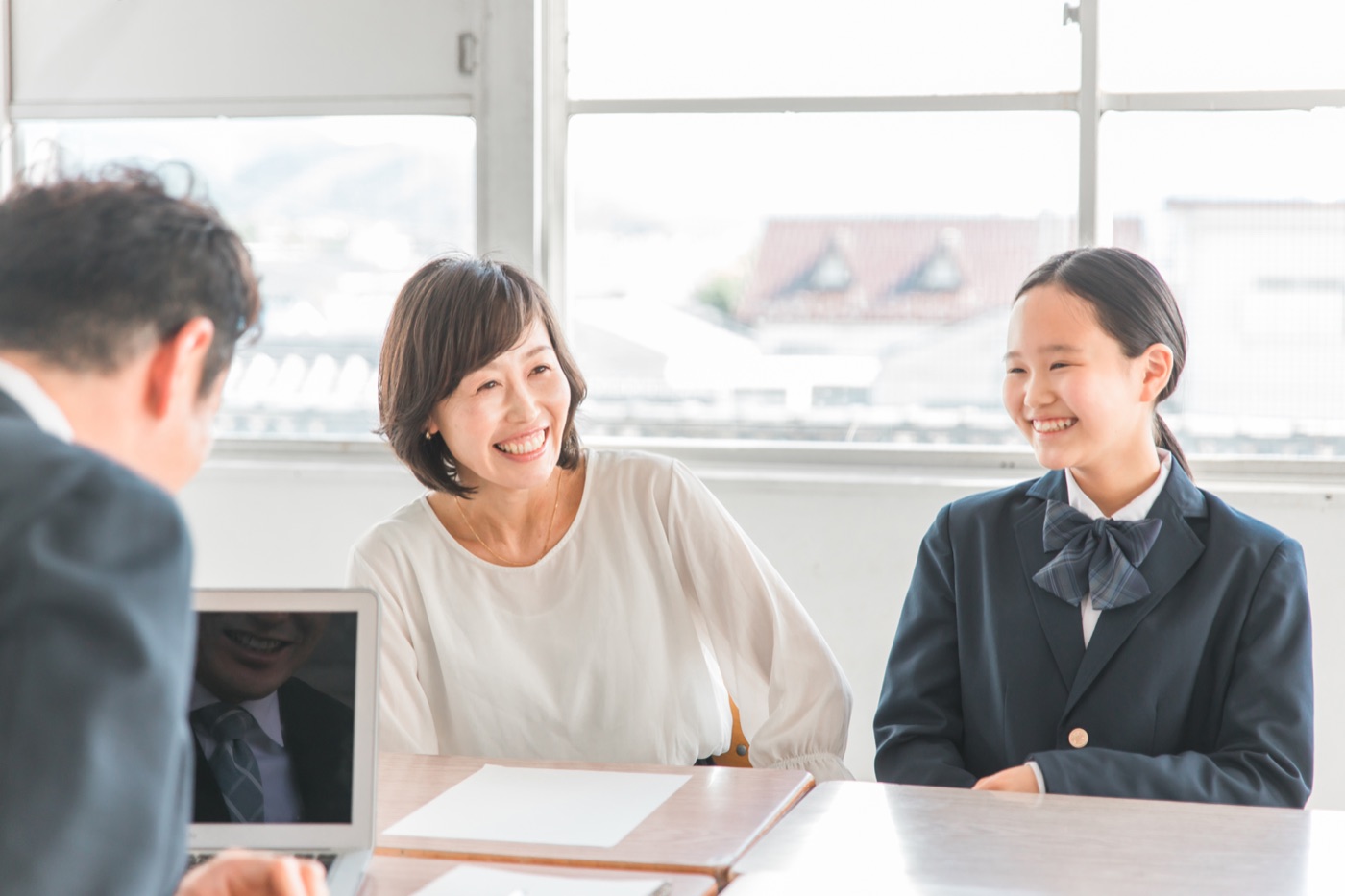 学校の一室で先生の説明を聞き、笑顔で話す母親と制服姿の娘